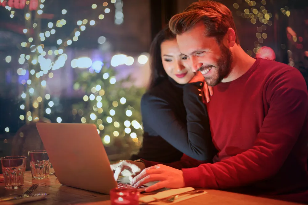 Eine Frau und ein Mann schauen lächelnd auf einen Laptop