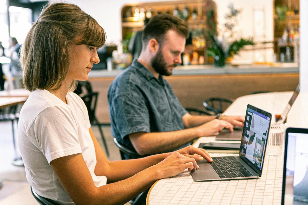 Eine Frau und ein Mann sitzen gemeinsam am Schreibtisch und arbeiten an Ihren Laptops