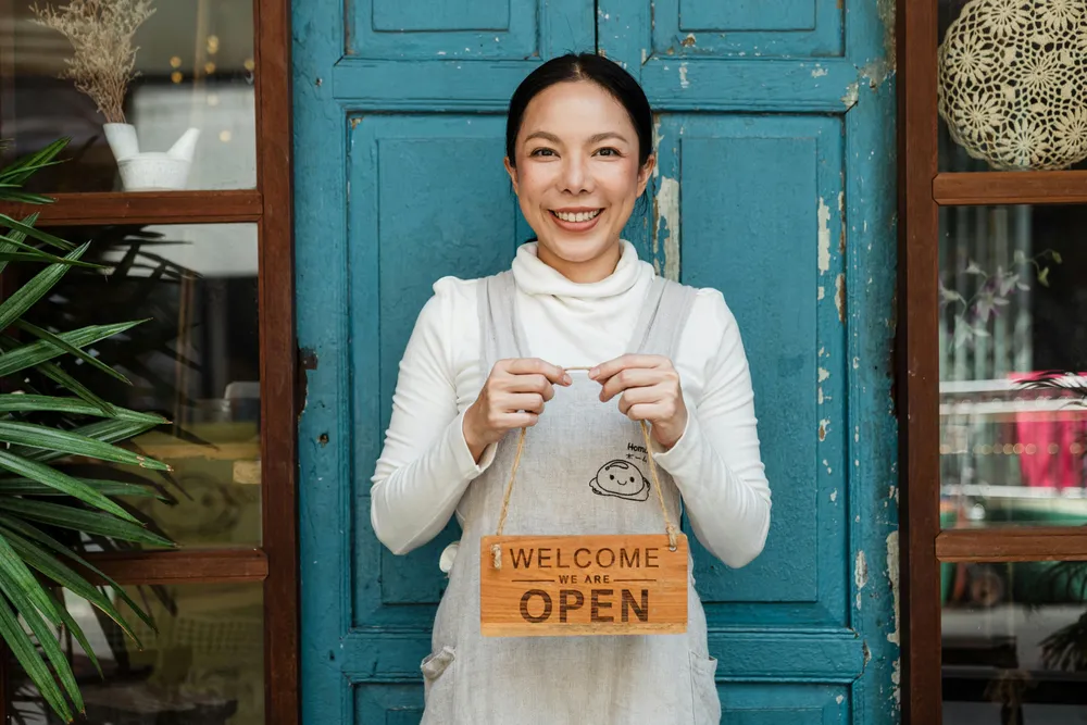 Eine lächelnde Frau hält ein Schild mit der Aufschrift 'Welcome we are open'