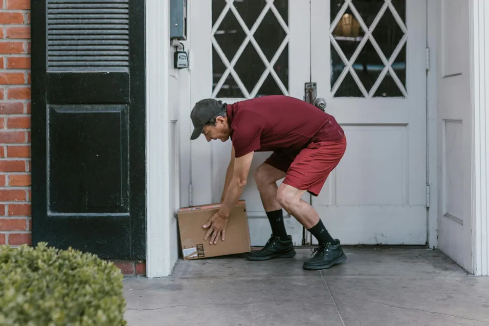 Ein Paketzusteller stellt ein Paket vor einer Haustür ab