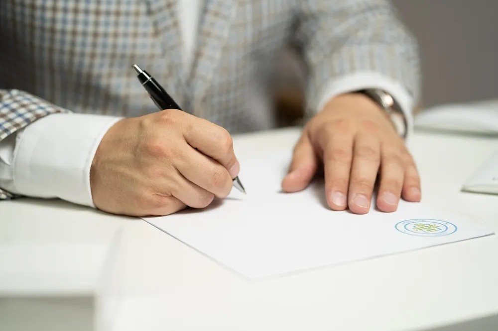 Ein Mann sitzt am Schreibtisch und schreibt auf ein Blatt Papier.